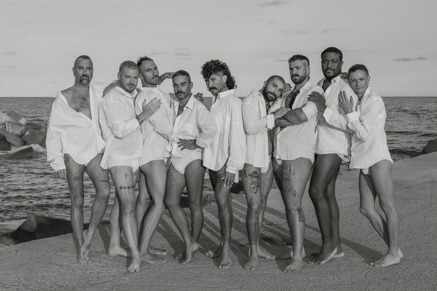 Group of people in white clothing posing together on a beach at sunset.