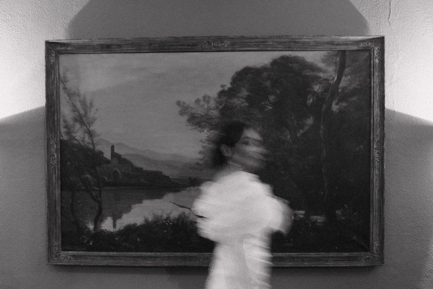 A series of landscape paintings hang in a gallery with a blurred figure moving through the frame.