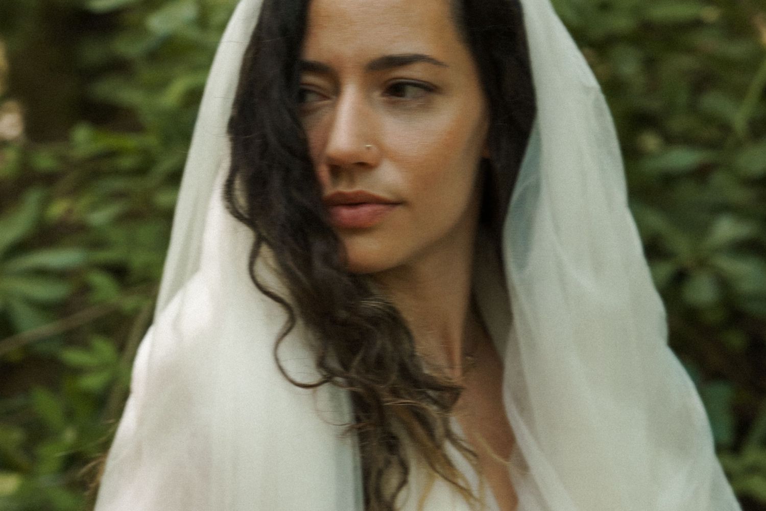 Side profile portrait of person wearing white bridal veil in garden setting.