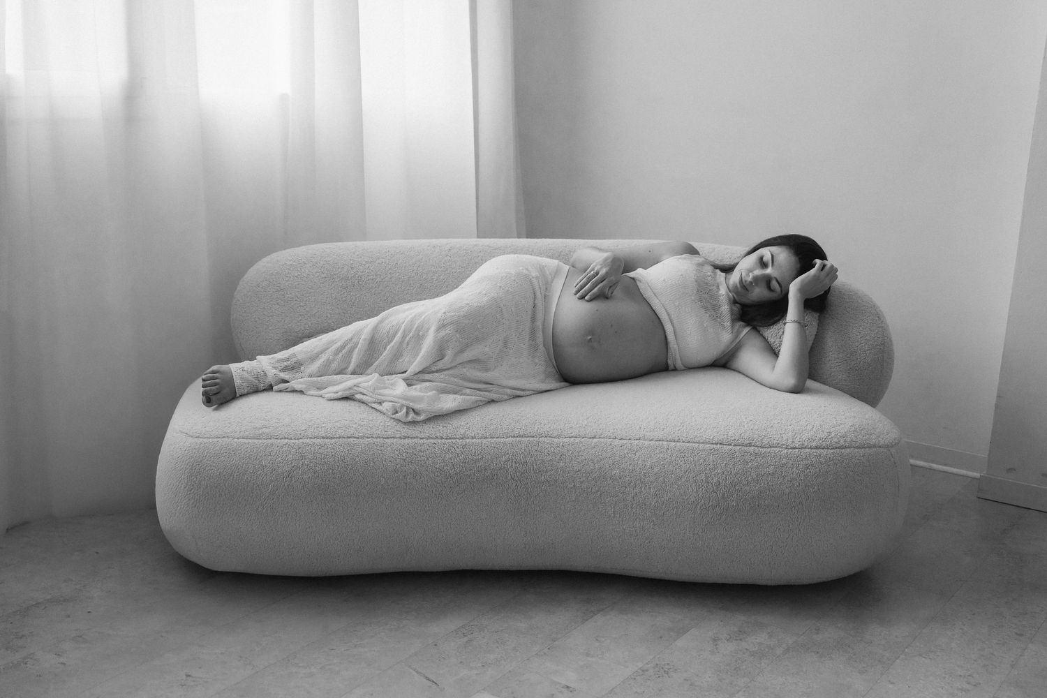 Artistic black and white photo of person reclining on white furniture.