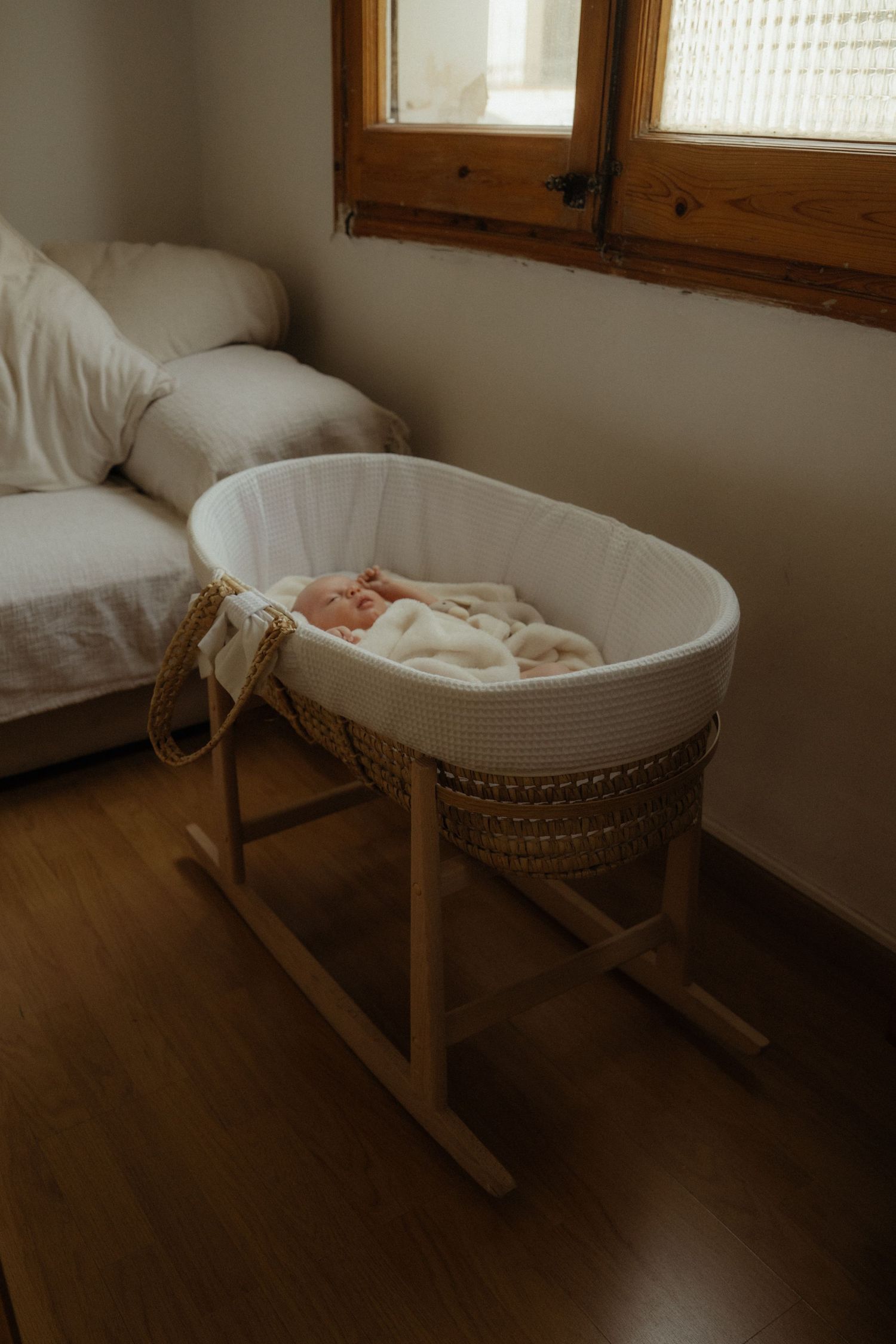 White wooden bassinet with rocking base sits in a sunlit nursery room.
