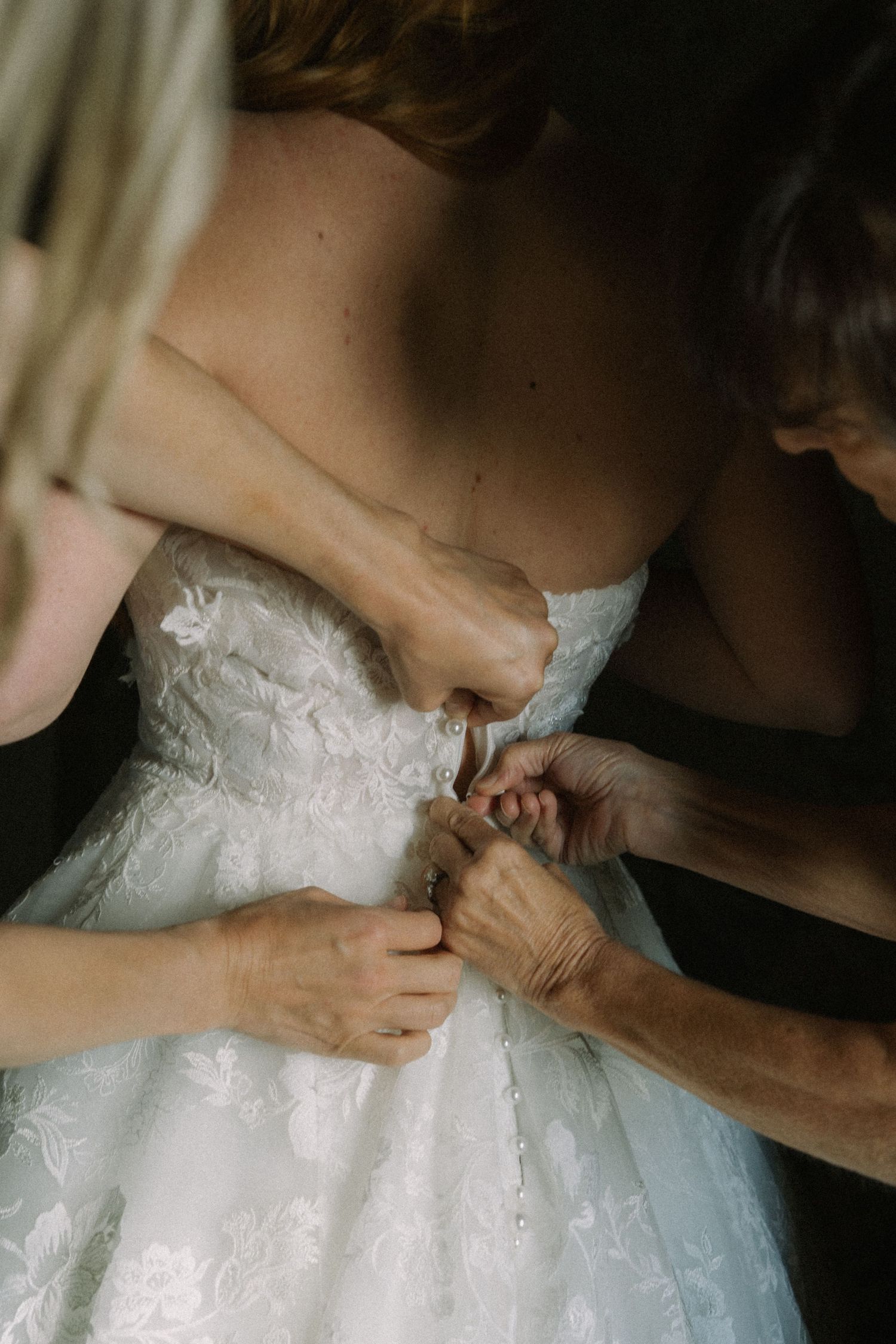 Close-up shot of hands lacing up the back of a white lace wedding dress.
