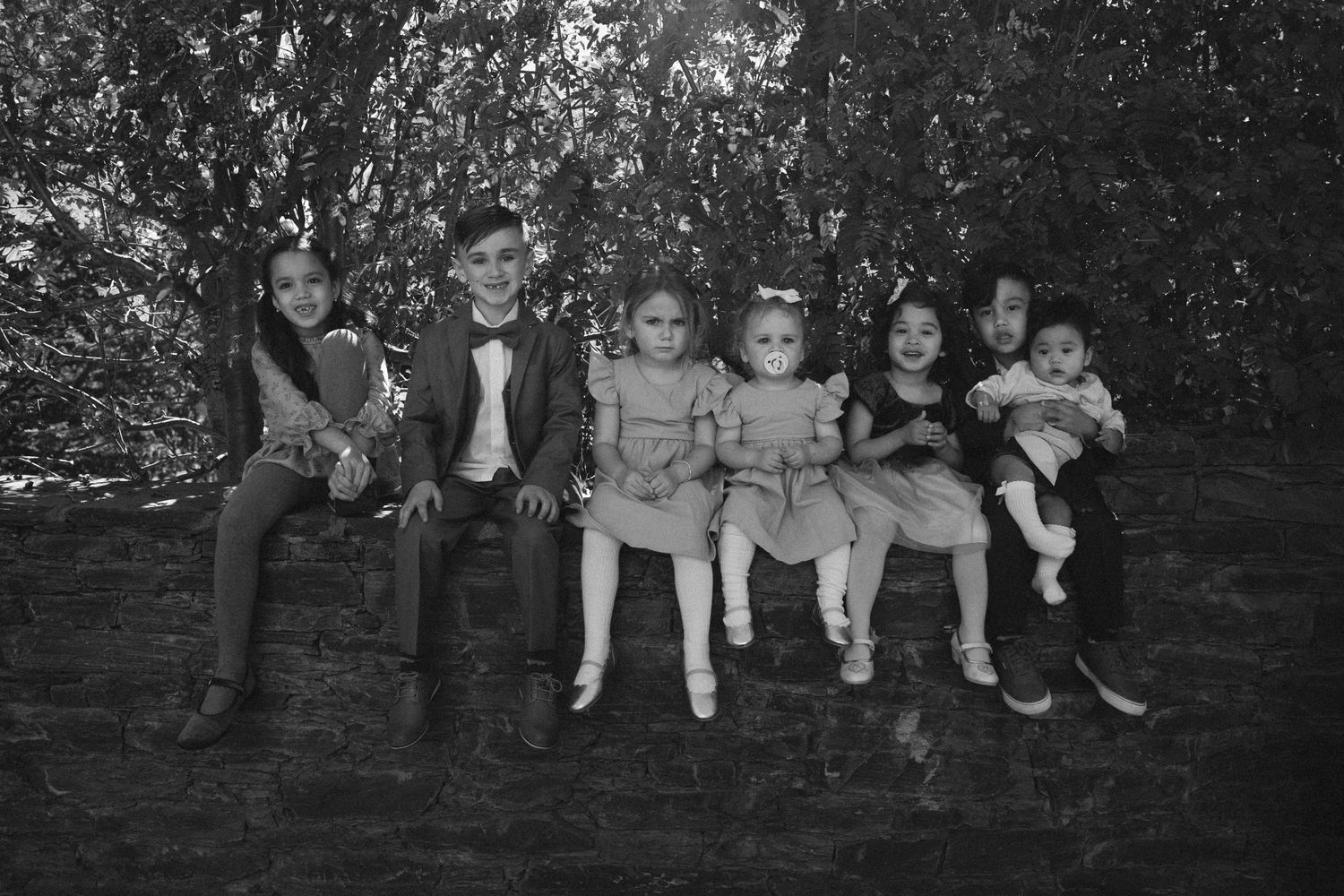 Black and white portrait of a family group sitting together outdoors on a log.