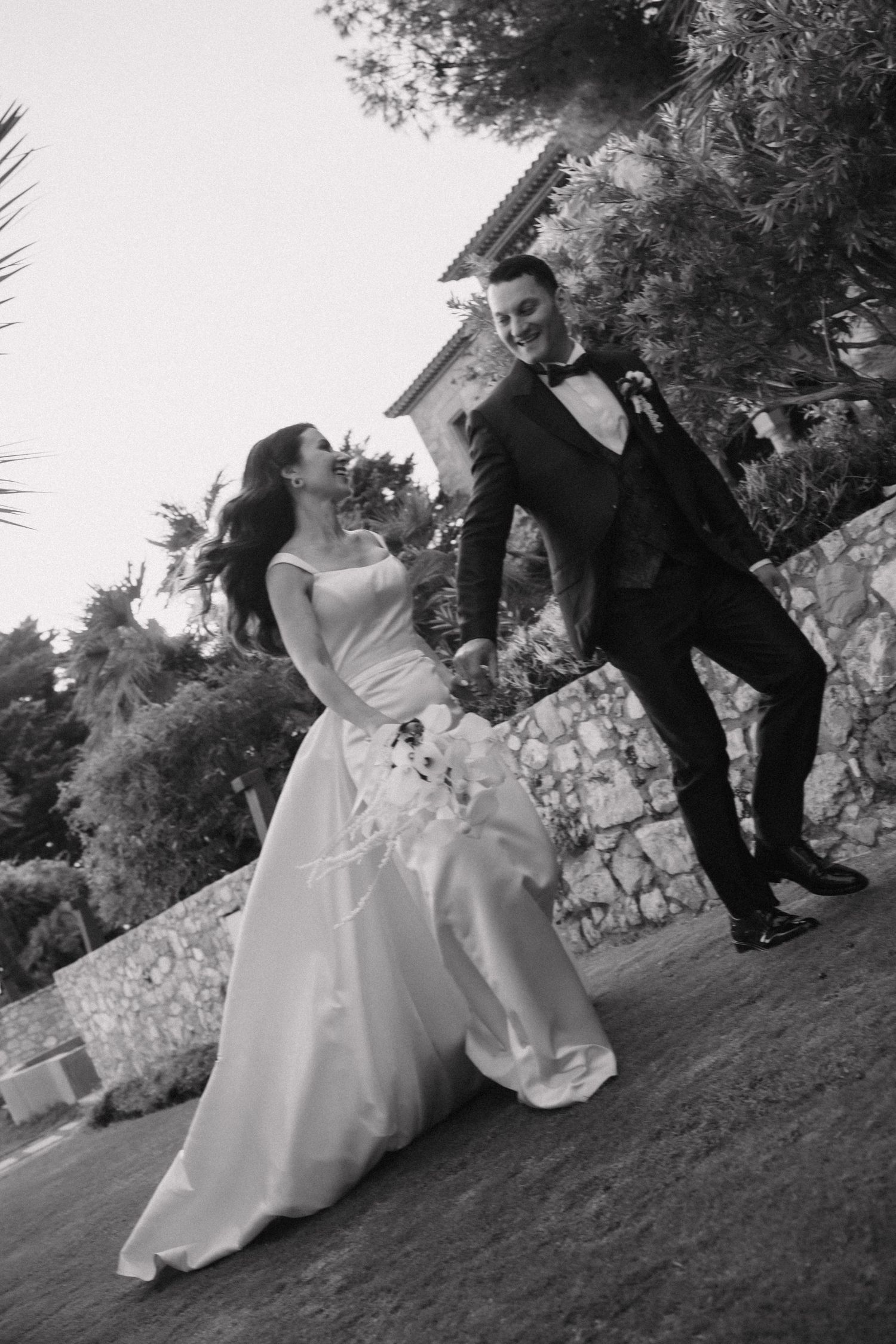 Playful black and white wedding photos of couple rolling on grassy hill.