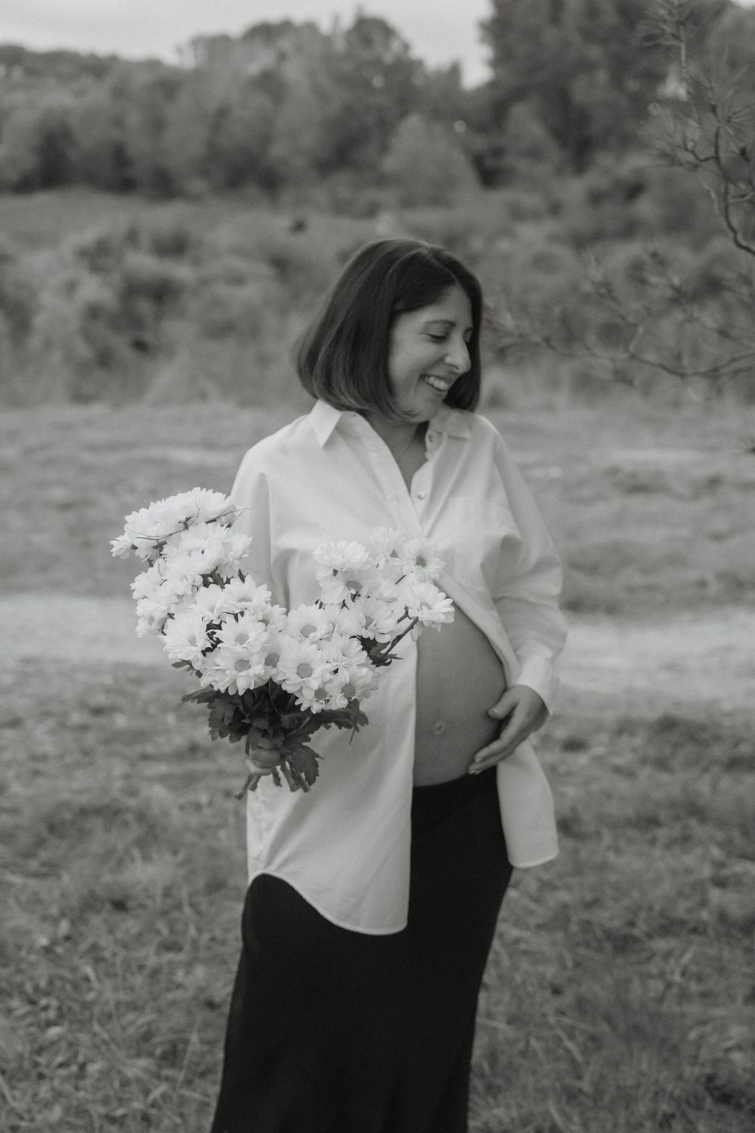 Person in black and white outfit holding white chrysanthemums in a field.