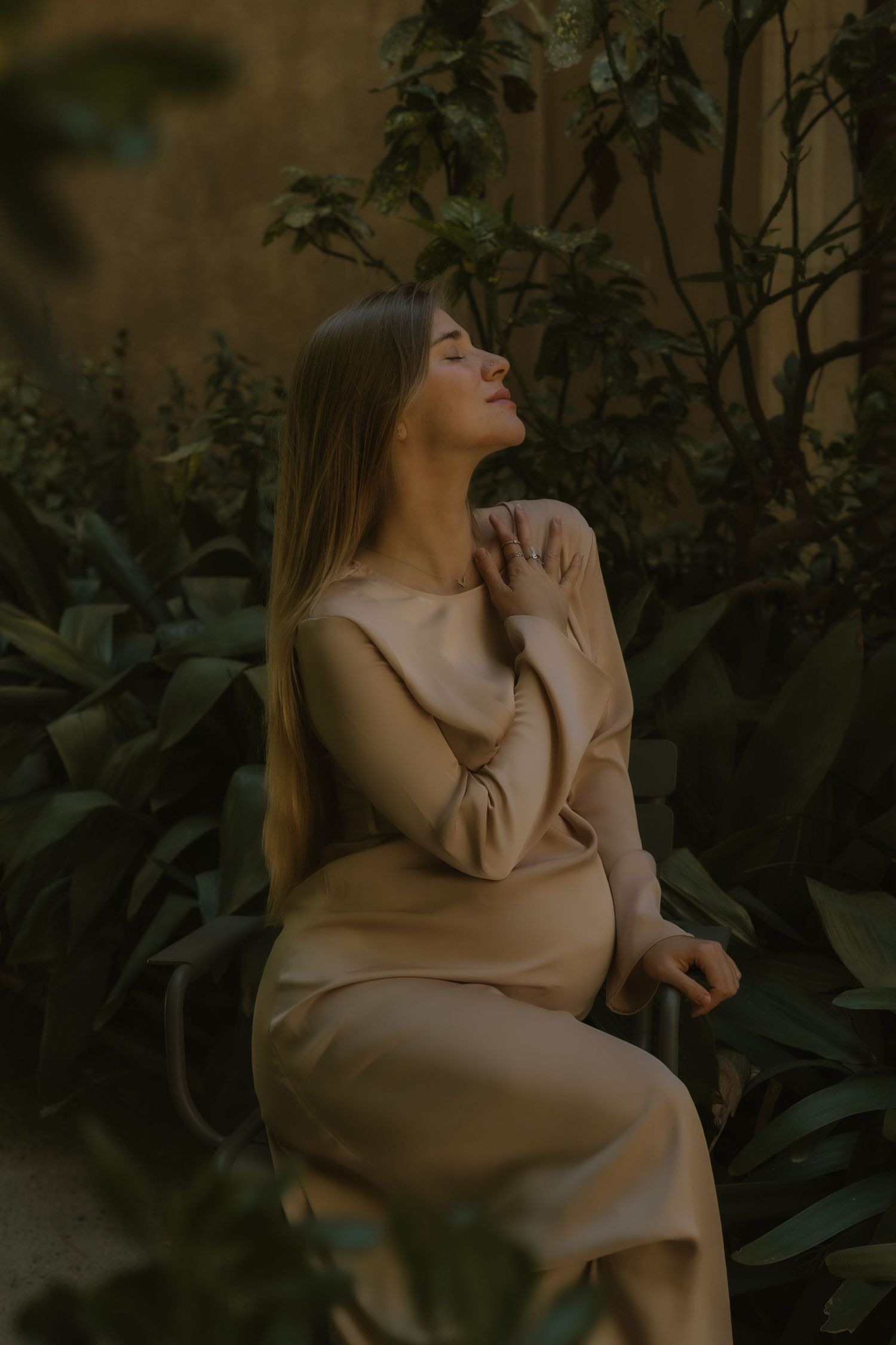 Artistic portrait in beige clothing against dark foliage background.