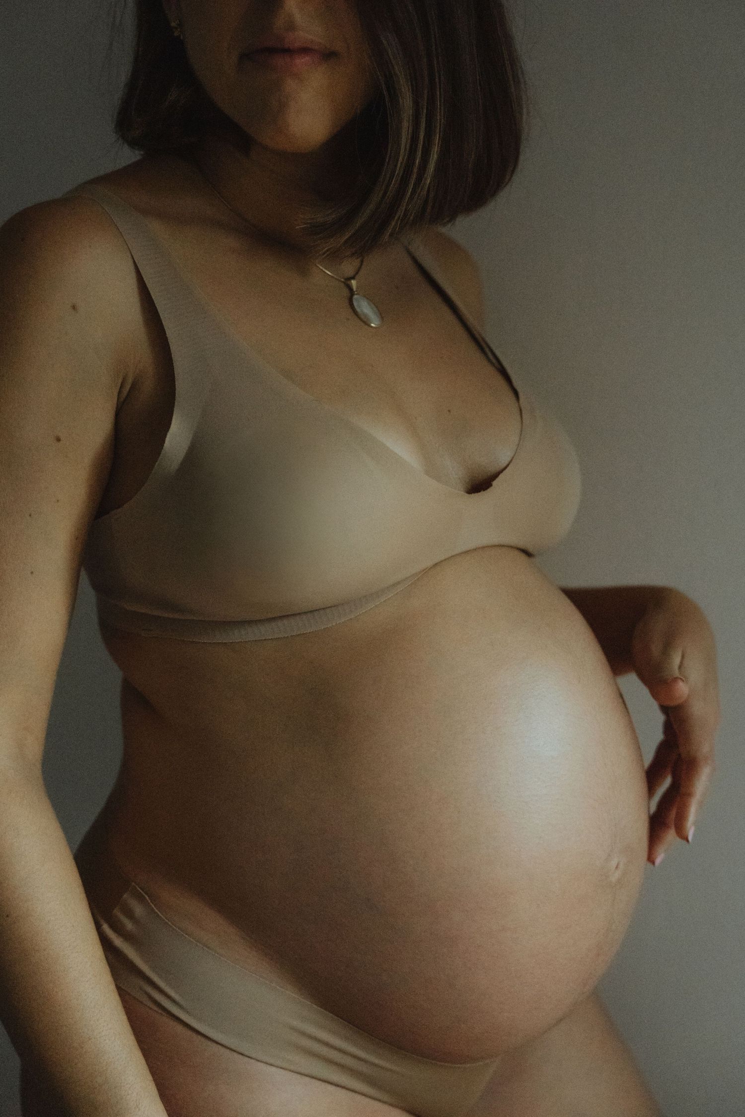 Side view of a pregnant belly in neutral-colored maternity wear.
