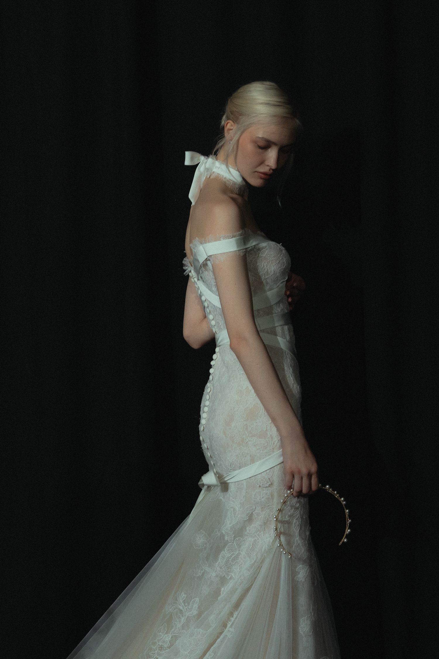 Ethereal bridal portrait featuring off-shoulder white lace gown against dark backdrop.
