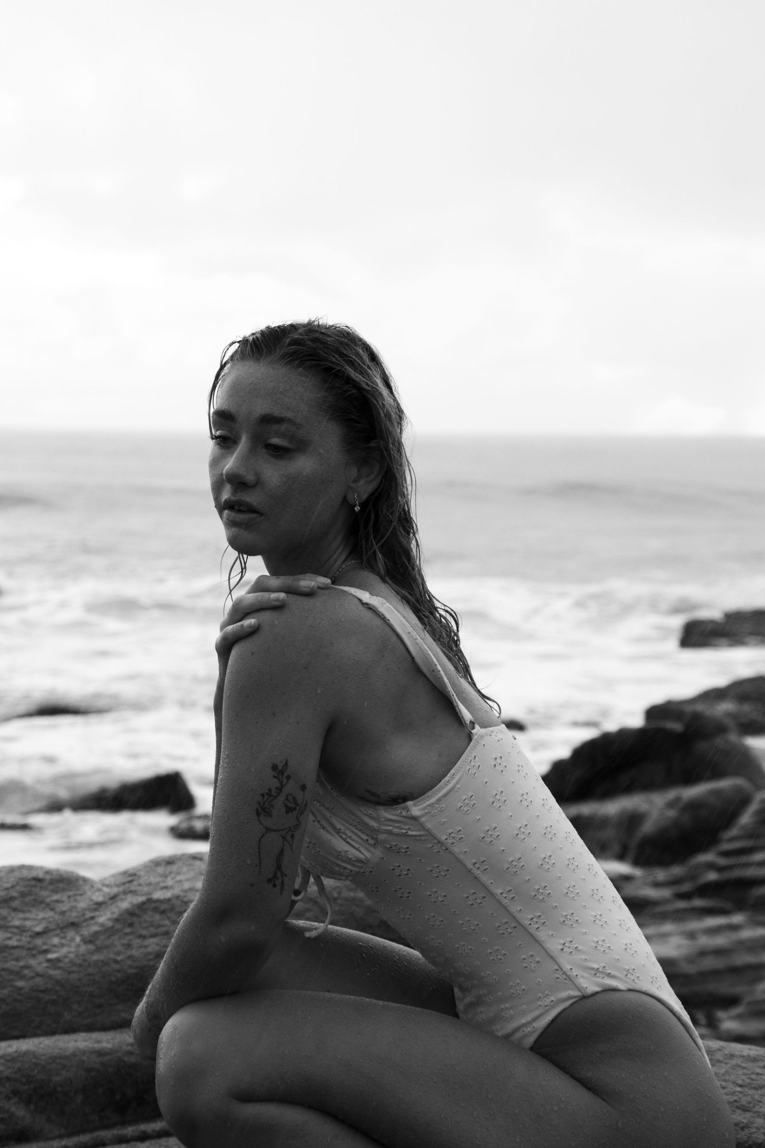 Person reclining on rocky shoreline in casual attire with ocean backdrop.