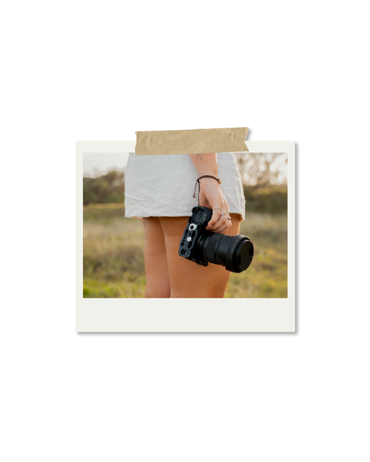 Woman in white dress holding a professional DSLR camera outdoors in a natural field setting.