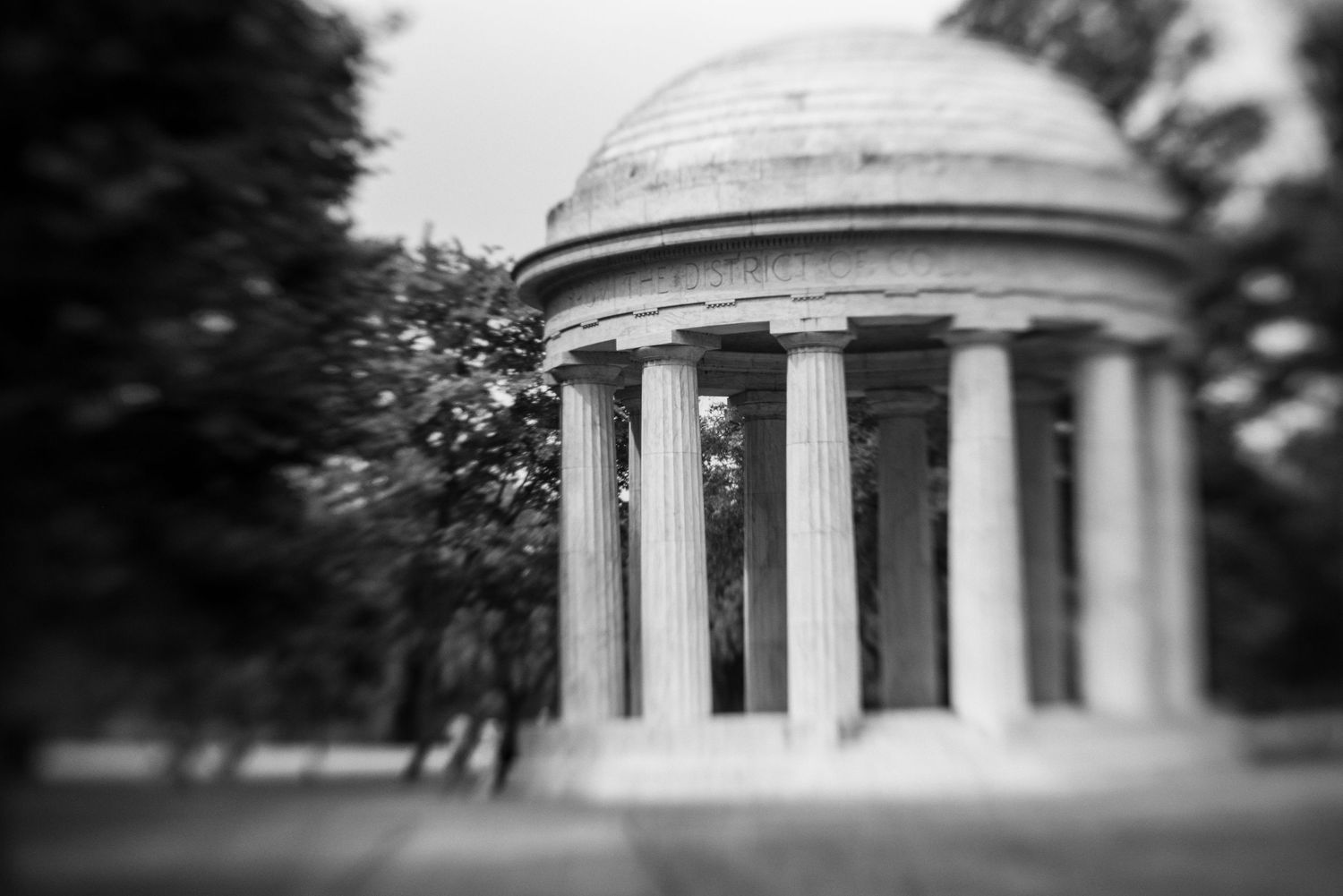 Black and white photo of the DC War Memorial rotunda with classical columns surrounded by trees.