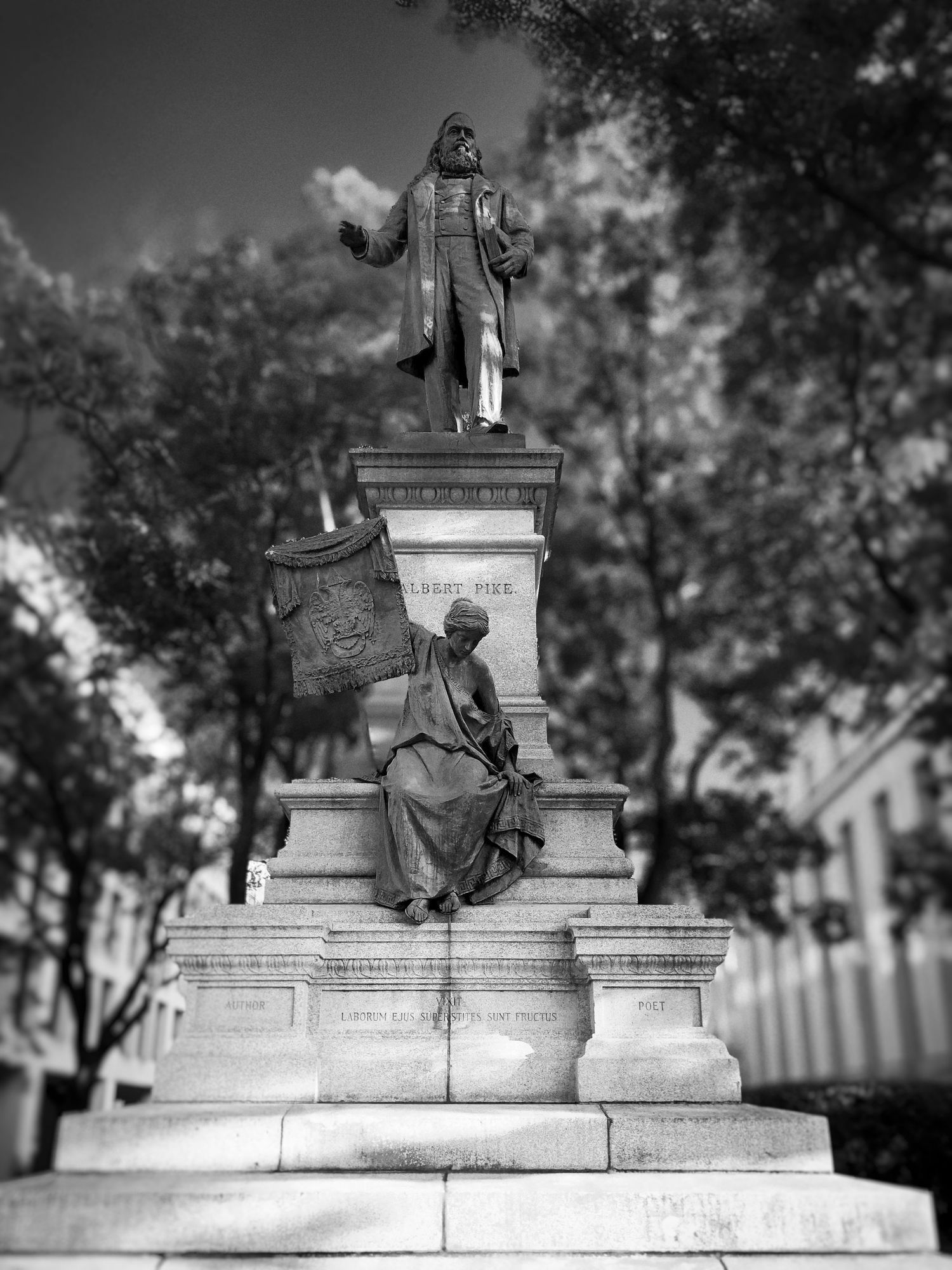 Black and white monument featuring a standing figure atop a pedestal with a seated figure below.