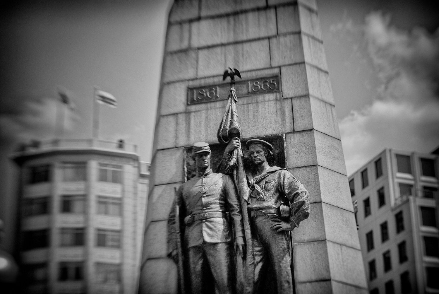 Black and white photo of a war memorial monument with bronze soldier statues holding a flag.