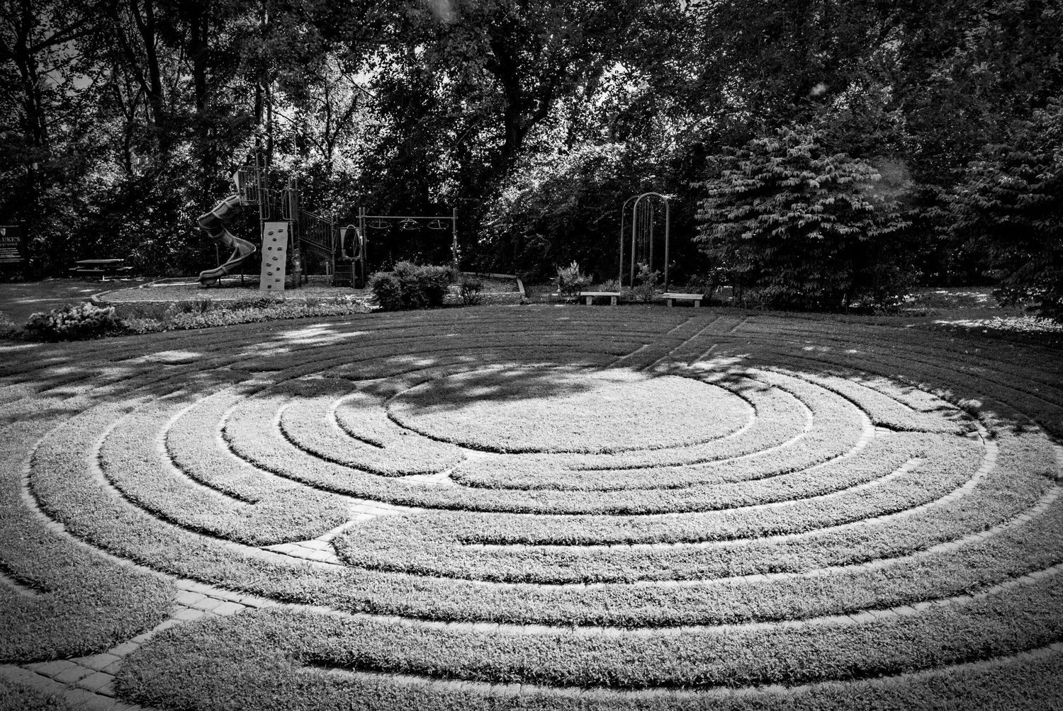 Aerial view of a circular stone labyrinth path surrounded by green grass and trees in a garden setting.