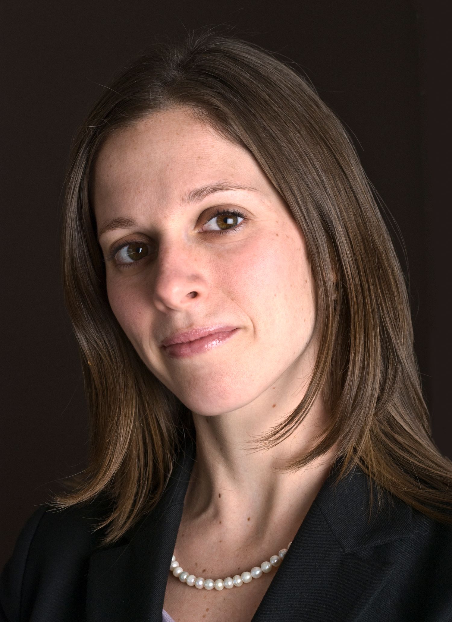 Elegant portrait of woman featuring pearl necklace and dark attire against black backdrop.