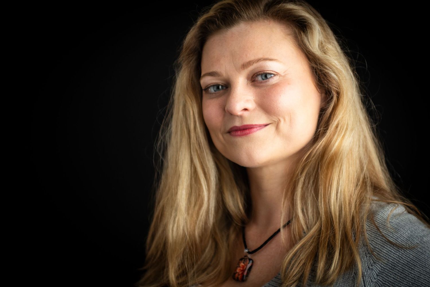 Professional headshot portrait of a woman in a blue top against a dark background.