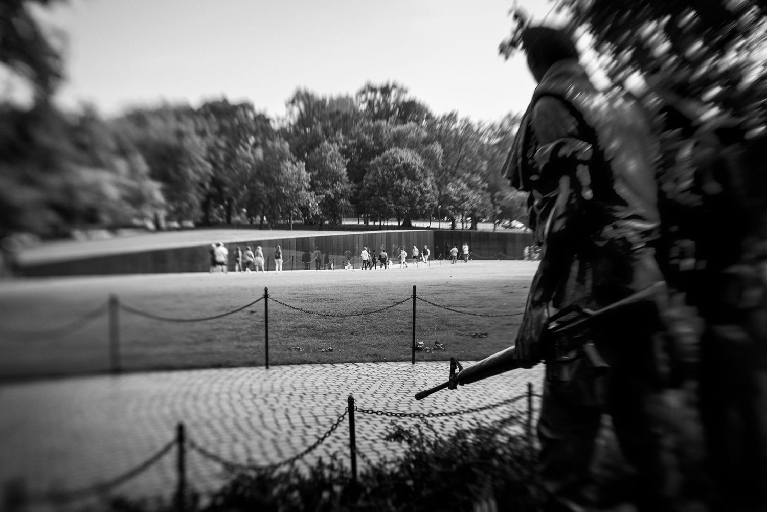 Black and white photo of a soldier statue near the Vietnam Veterans Memorial Wall.