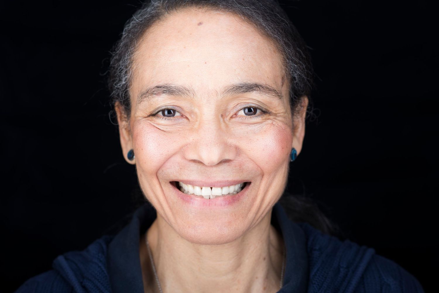 expressive headshot showing a Woman in dark attire against black background.