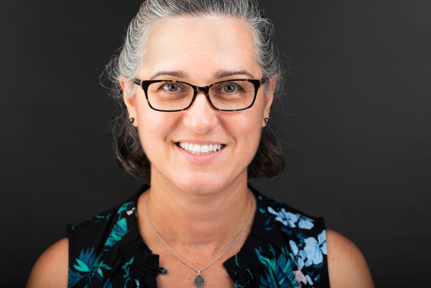 Portrait of a woman in floral top wearing glasses against dark background.