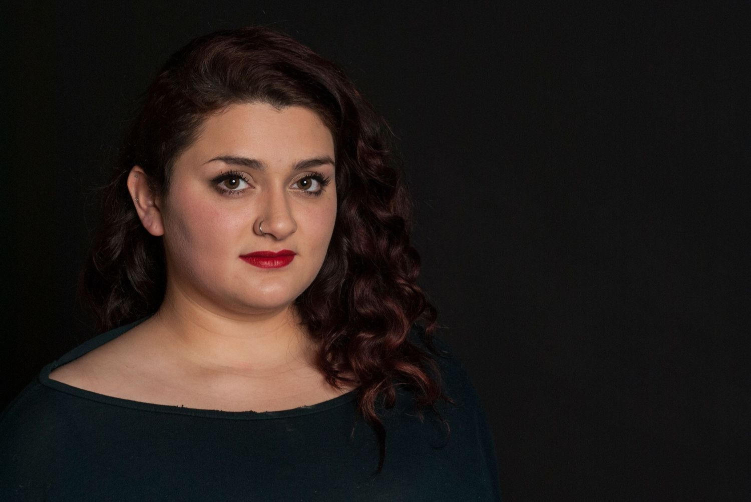 portrait of a young woman with dark curly hair and red lipstick against dramatic black backgrounds.