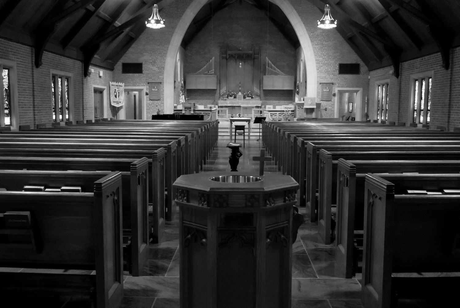 Interior view of an empty church sanctuary with wooden pews and traditional architectural details in black and white.