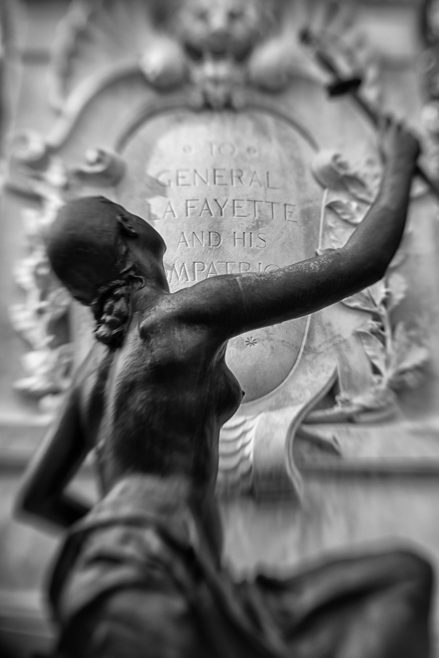 Black and white photo of a bronze female statue in front of a General Lafayette memorial monument.