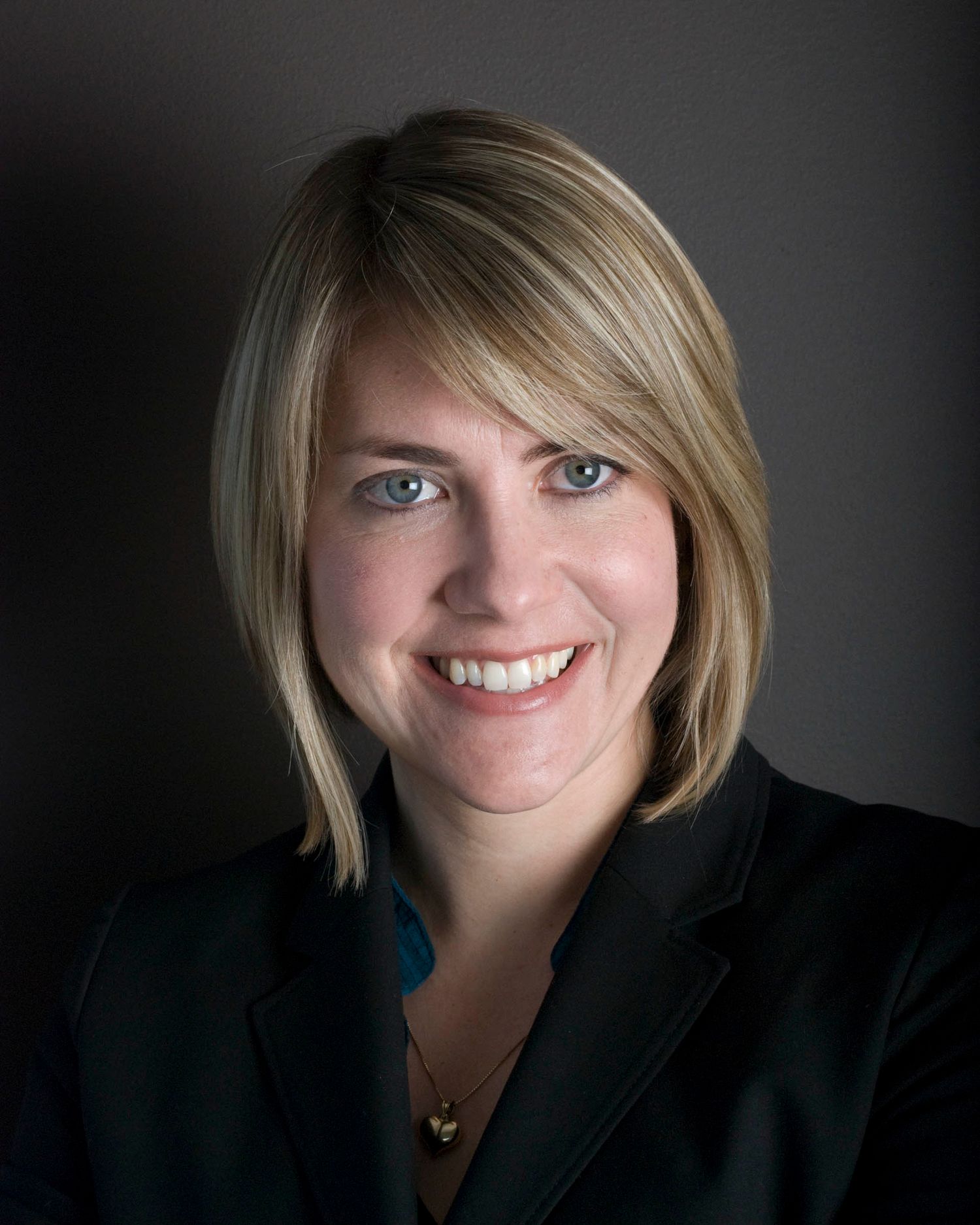 Headshot of young woman with blond hair and engaging blue eyes, again a gradient gray background