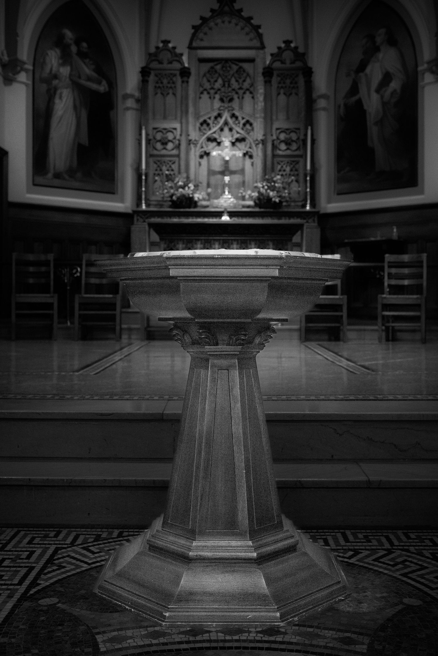 Stone baptismal font stands in front of an ornate church altar with gothic arches and religious artwork. John's Episcopal Church Georgetown