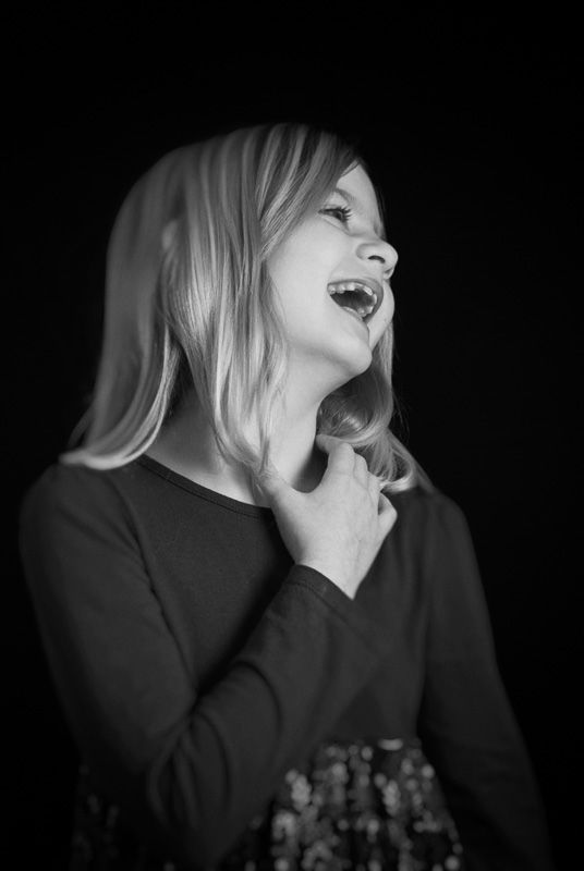 Expressive black and white portrait showing joyful laughter against dark background.
