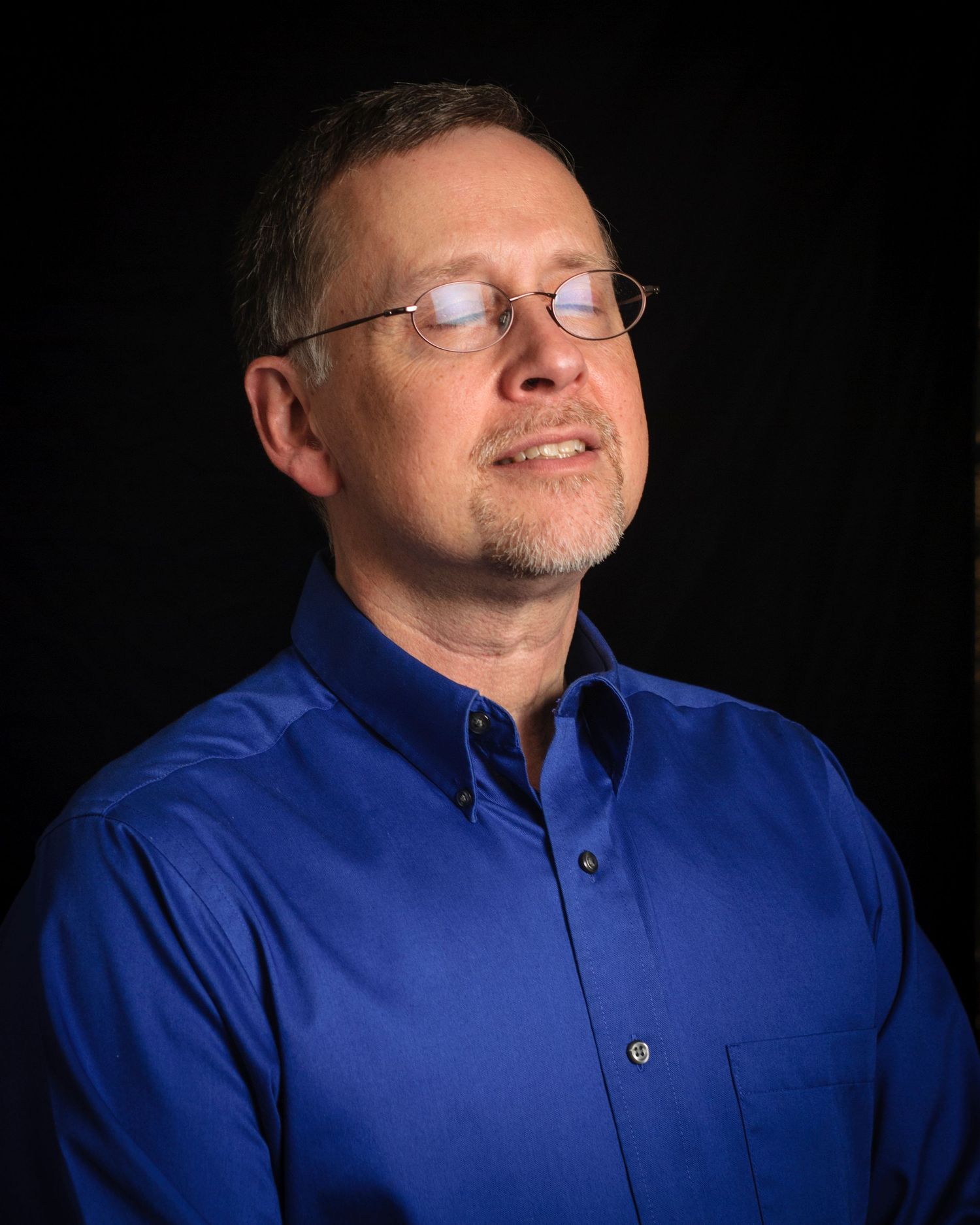 Headshots showing a man in a blue button-down shirt against a black background with looking towards the light with eyes closed.