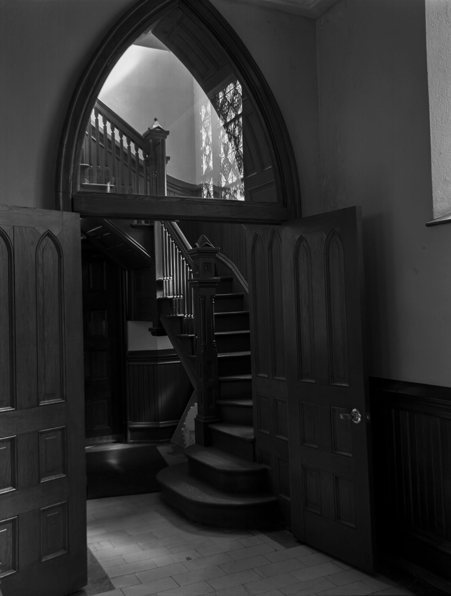 Gothic arched doorway reveals a curved wooden staircase in a historic church interior.