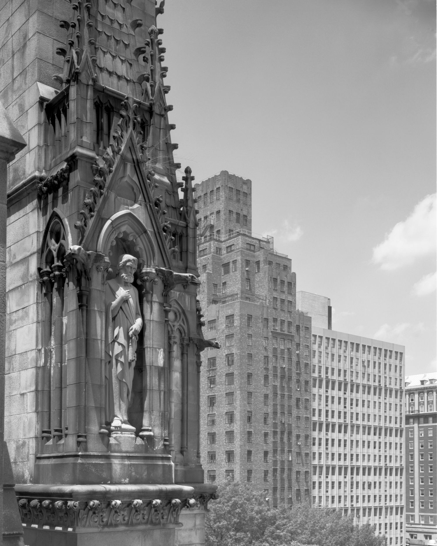 Detail of the Cathedral Church of St John the Divine north tower  against an urban backdrop of tall buildings in black and white.