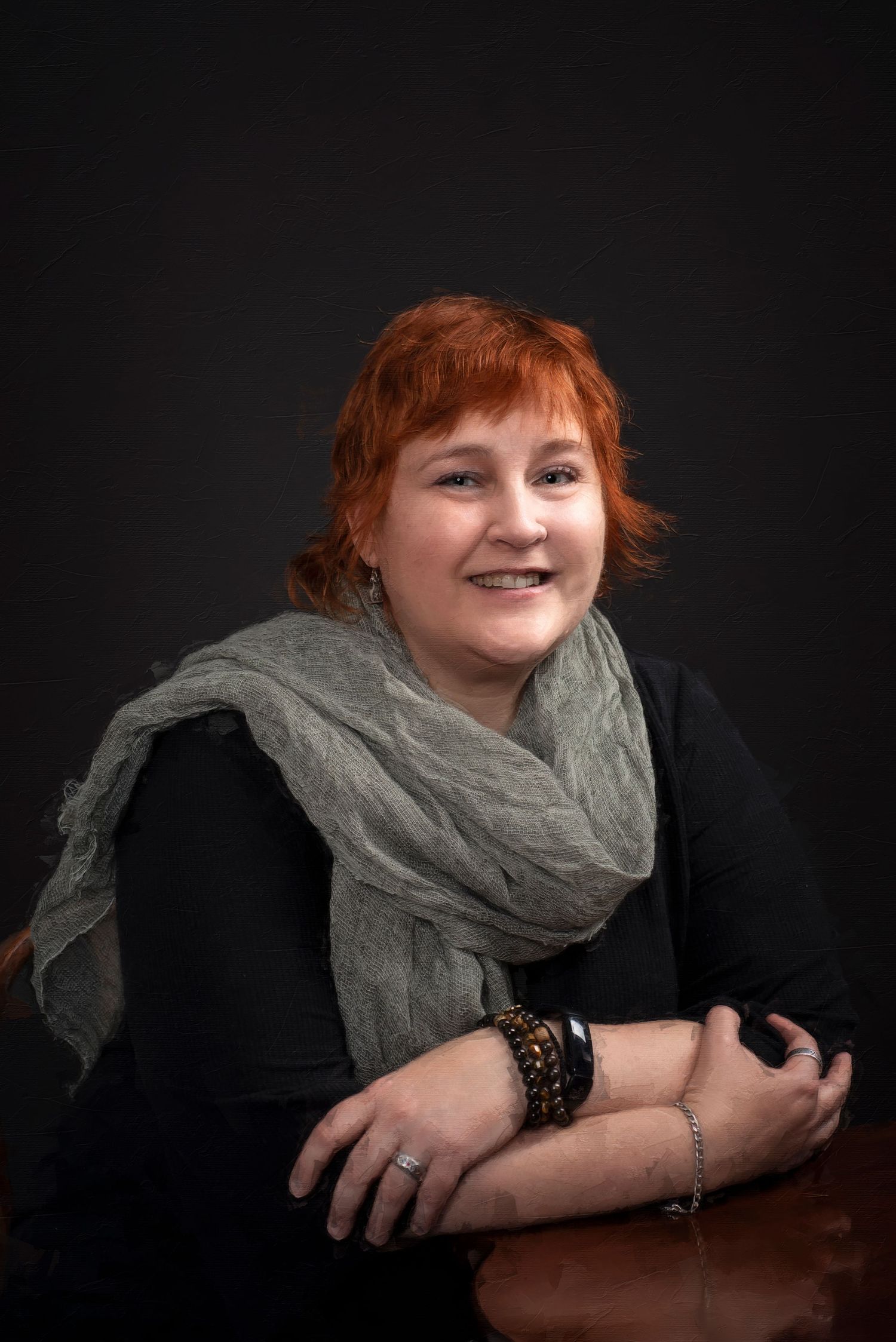 Studio portrait featuring woman wearing a gray green  scarf and black outfit against dark background.
