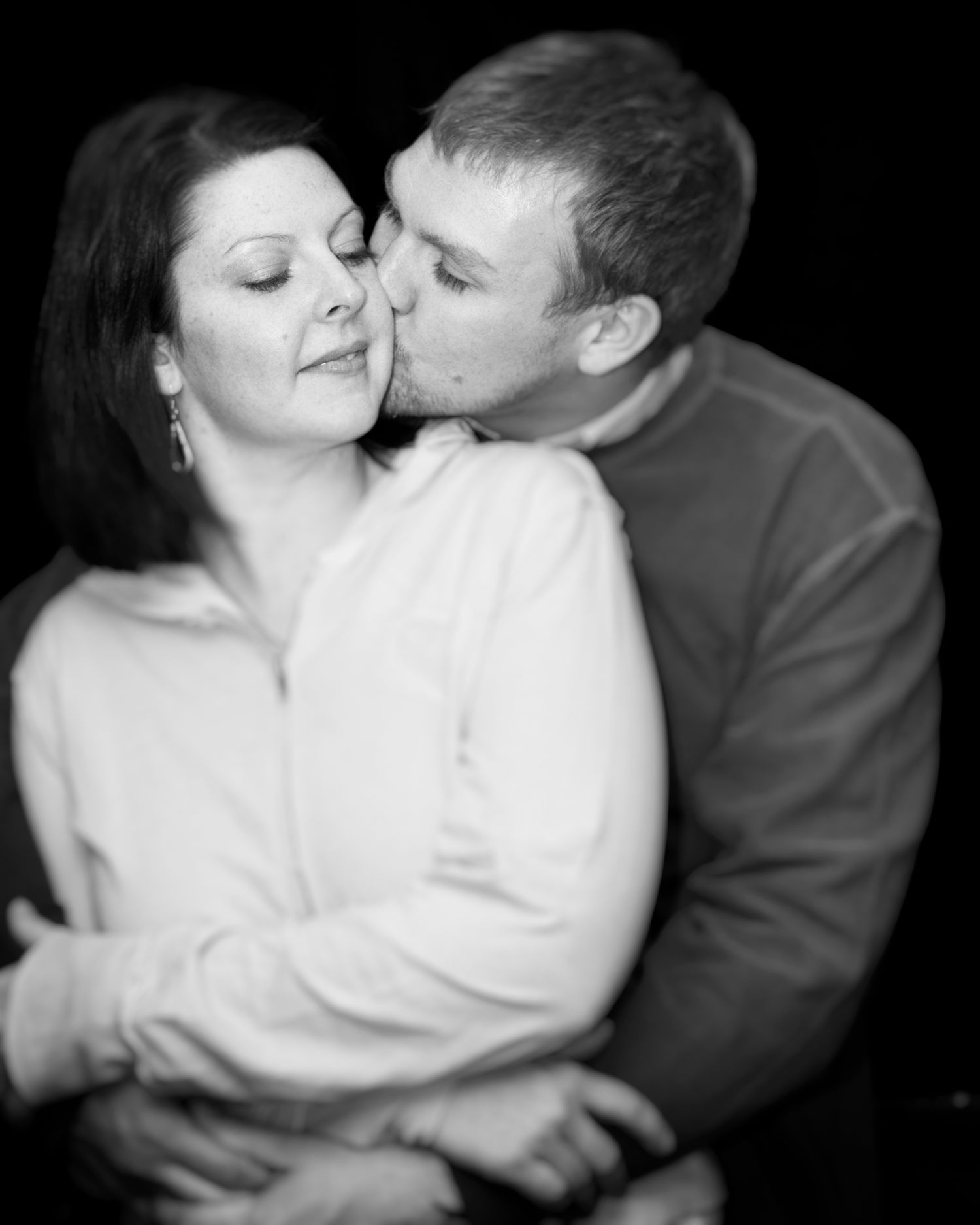 Black and white romantic portrait of a couple sharing an intimate moment against dark background.