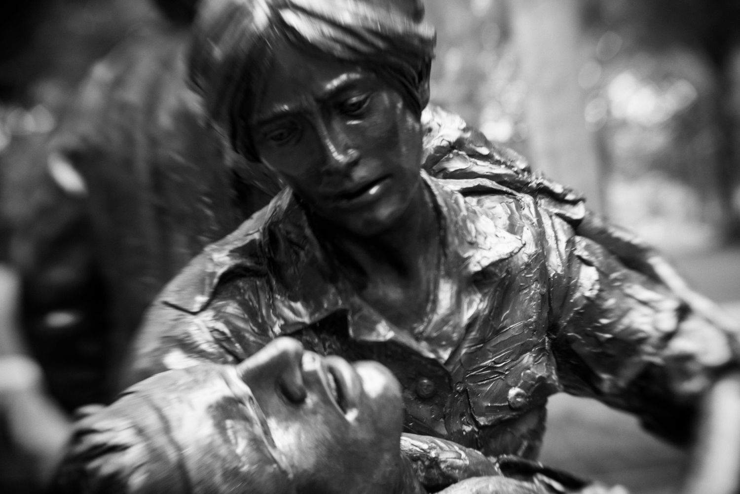 Black and white bronze statue of a soldier cradling a wounded comrade, depicting wartime sacrifice and compassion.