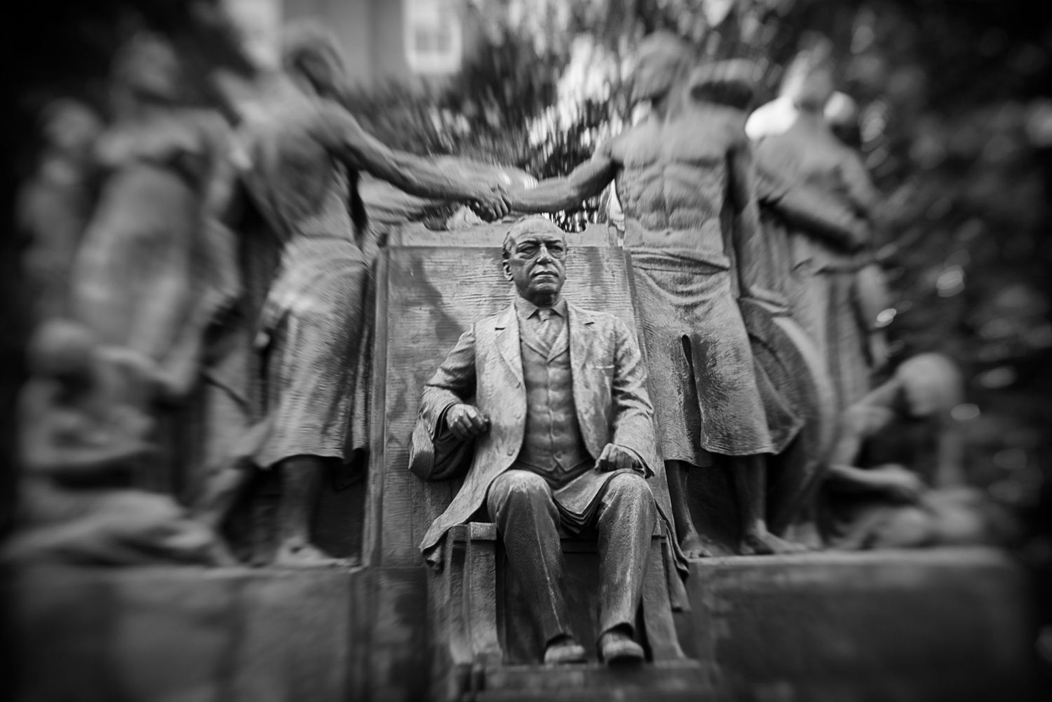 Black and white photo of a bronze memorial statue of a seated man surrounded by figures in relief.