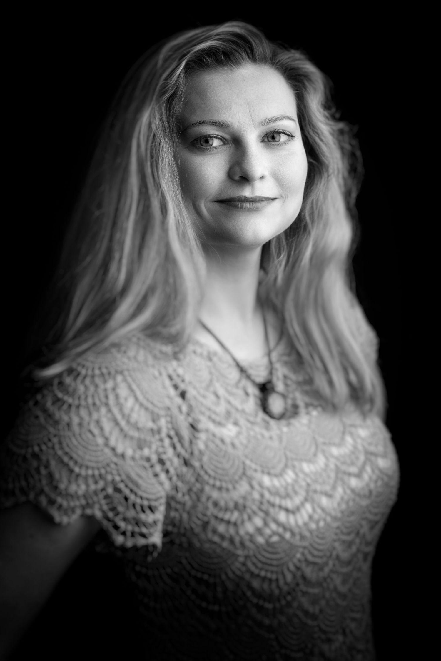 Dramatic portrait featuring young woman in delicate lace top against black background.