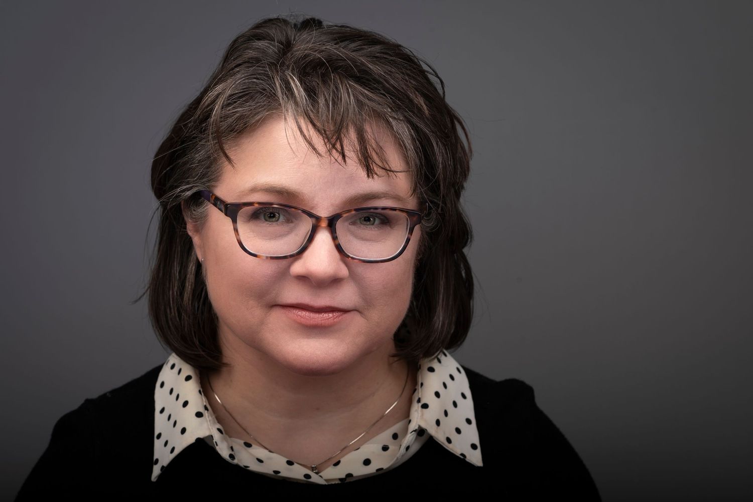 Studio portraits showing a woman wearing glasses and polka dot collar against dark background.