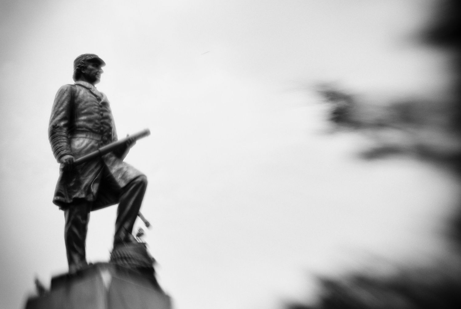 Black and white photo of a Civil War soldier statue holding a rifle, mounted on a pedestal against a cloudy sky.