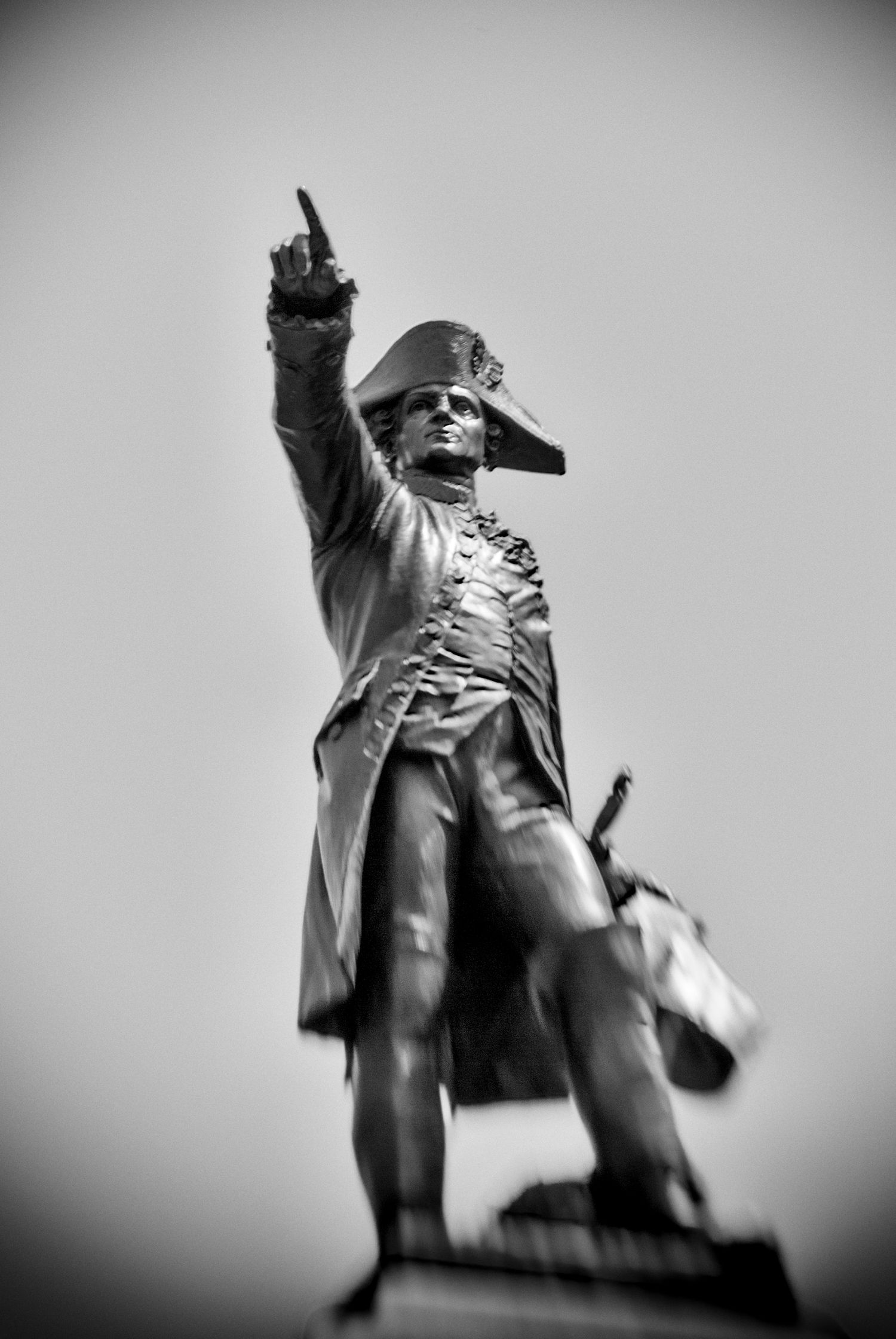 Black and white photo of a historic military statue with raised finger, wearing a bicorne hat and uniform.