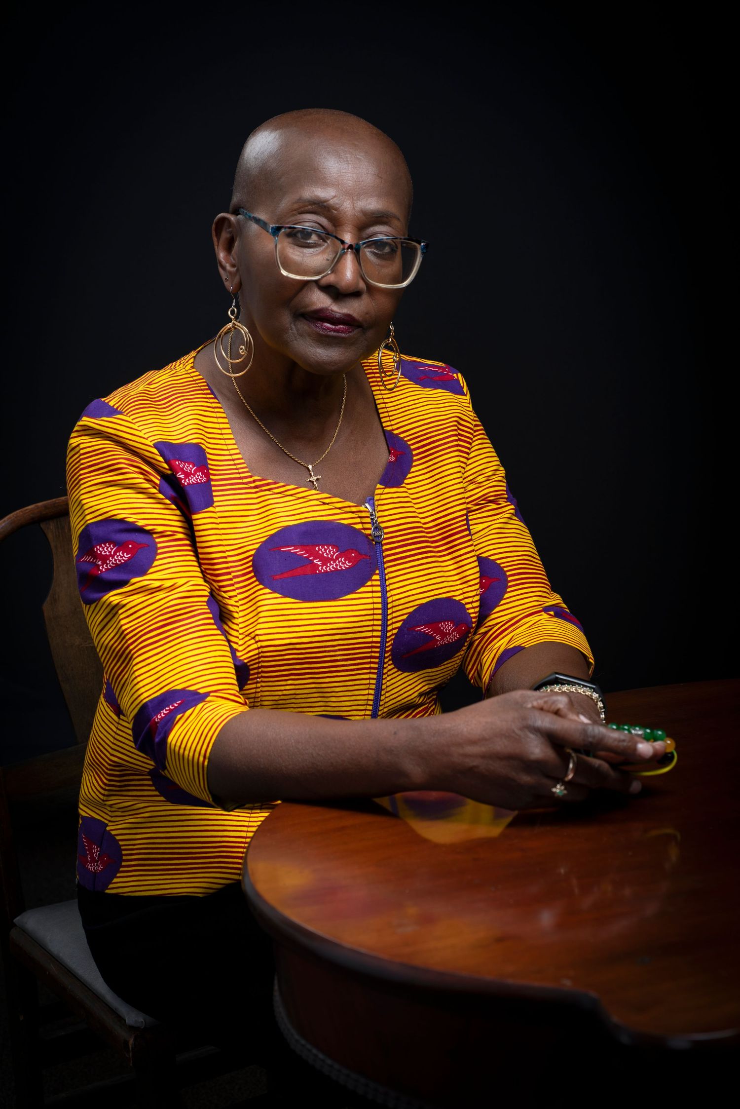 Portrait series showing a woman in bright yellow and purple traditional African dress siting at a table.