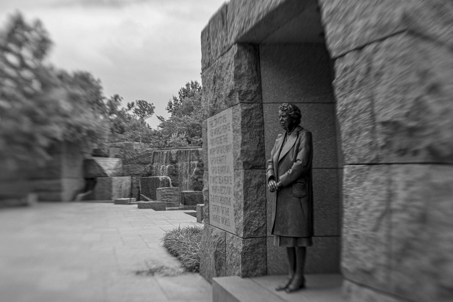 Black and white photo of a bronze statue of a woman standing in a stone alcove at the FDR Memorial in Washington, DC.