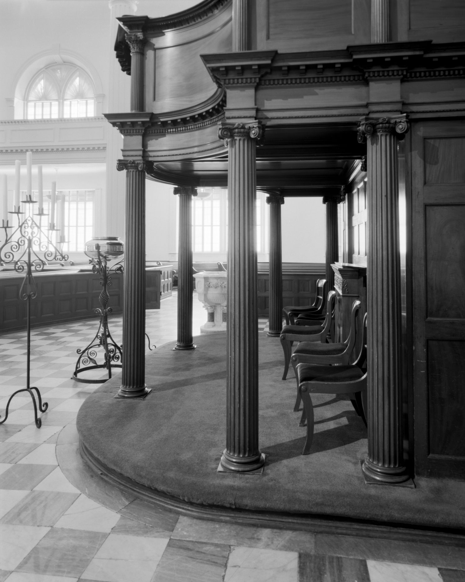 Interior church architecture showing curved wooden pews and classical columns in black and white.