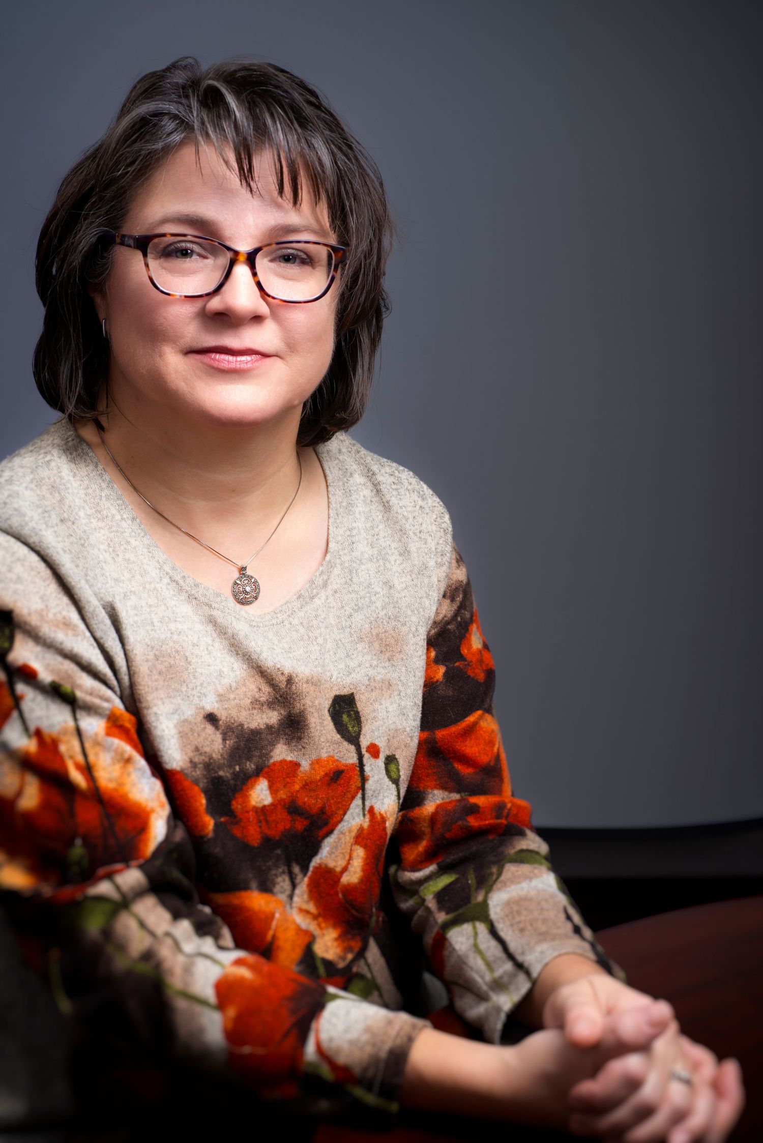 A person in glasses and a beige sweater poses with vibrant orange flowers against a dark gray background.