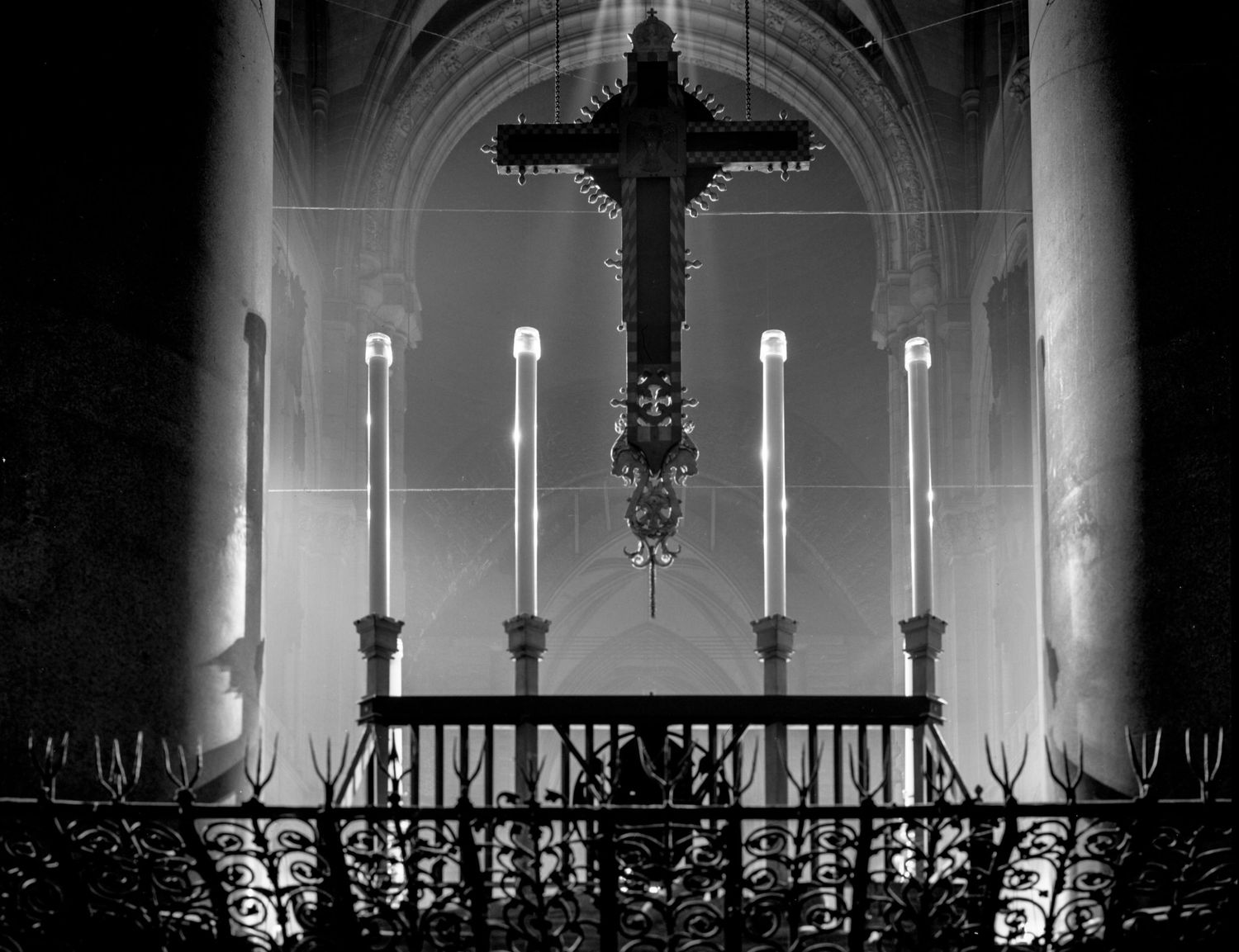 Dramatic black and white church altar view with illuminated candles and cross silhouetted against arched windows.