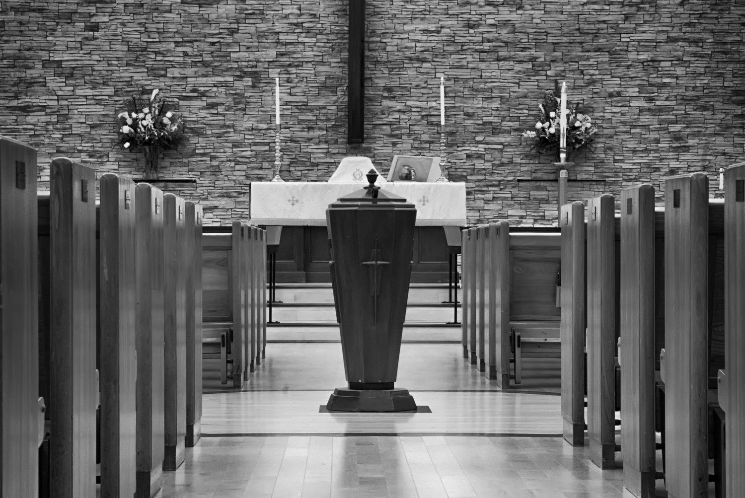 Interior view of empty church pews in black and white with stone walls and dramatic lighting down the center aisle.