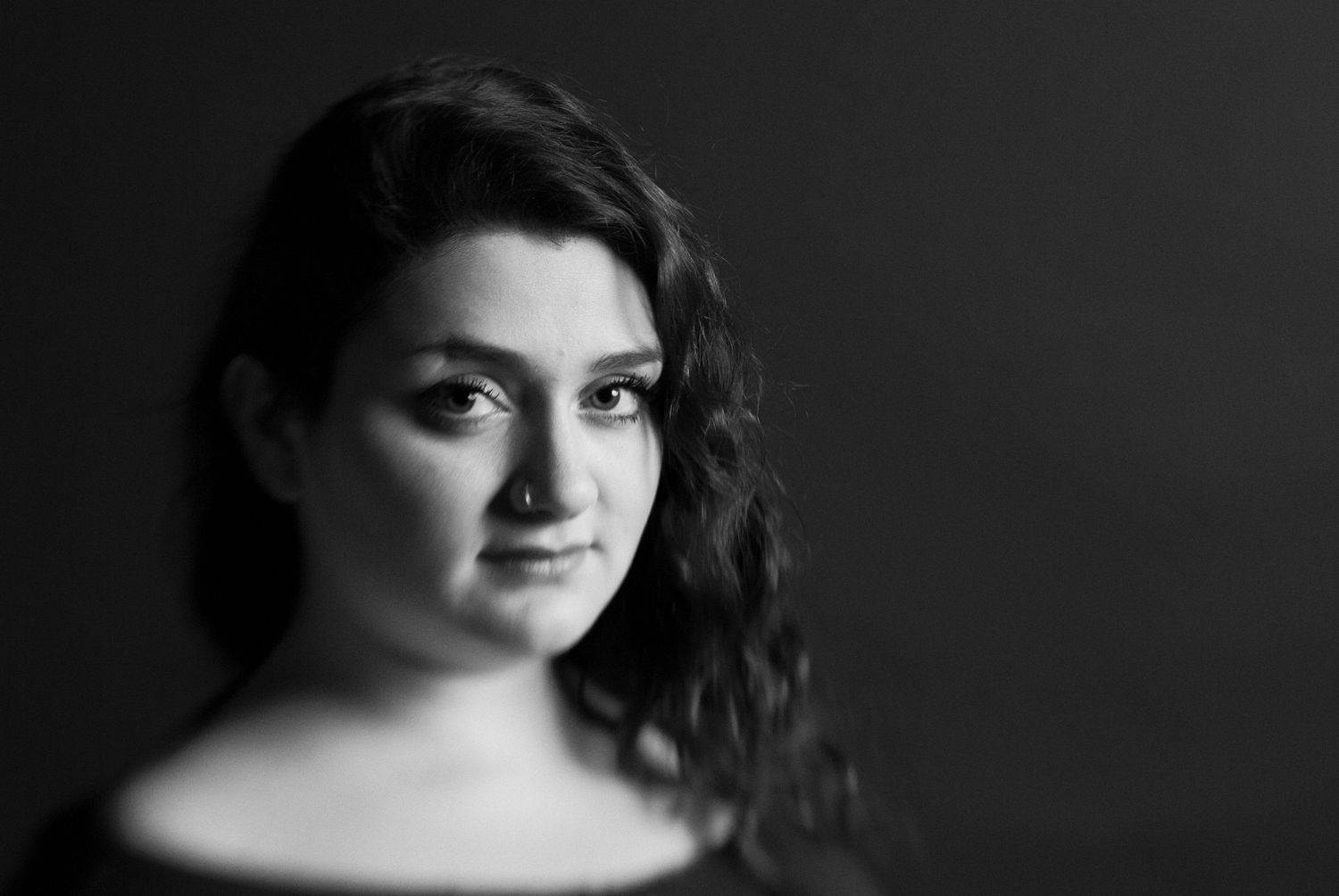 Dramatic black and white portrait of young woma with moody lighting and dark background.