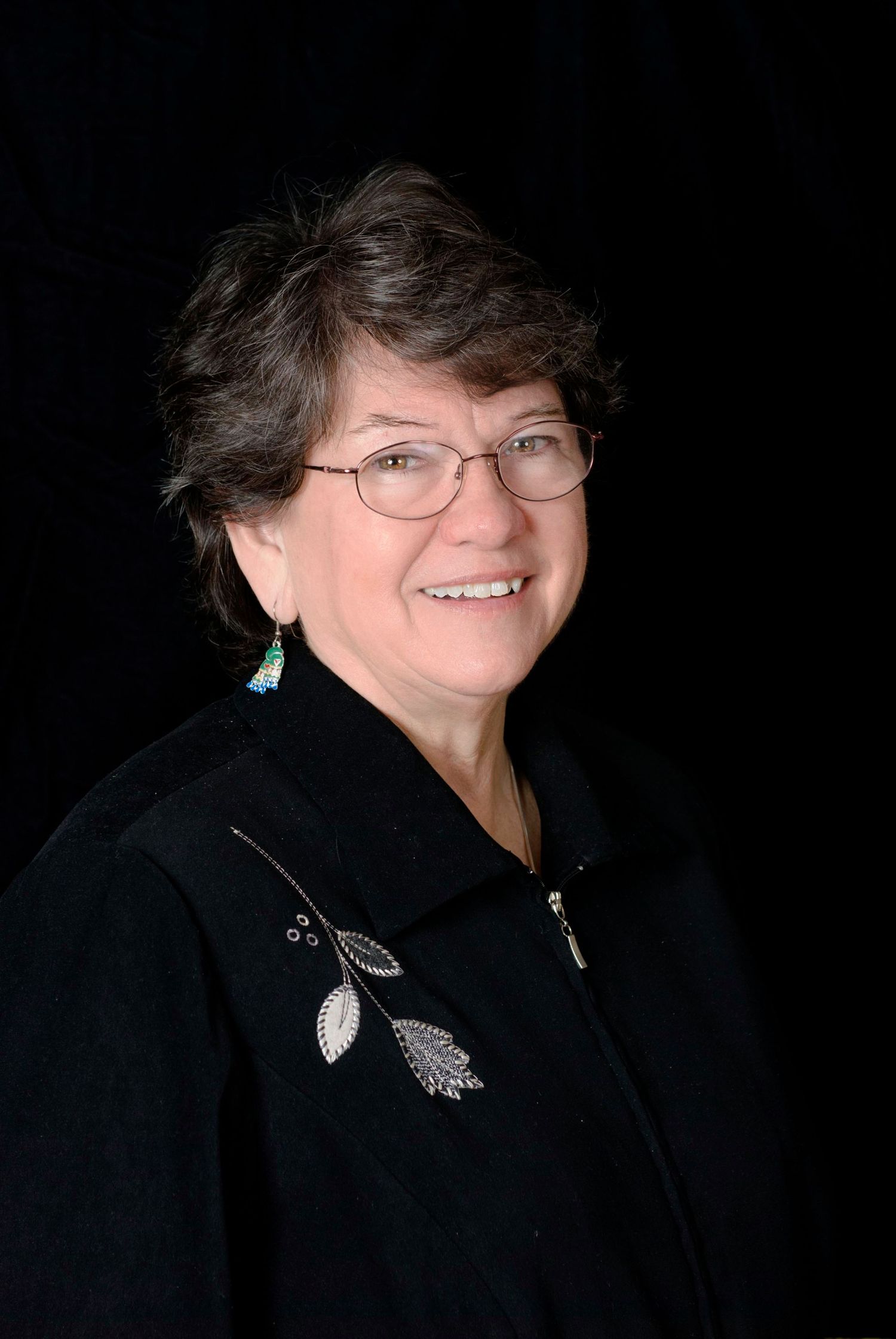 Portrait showing silver leaf brooch details on black jacket against dark background.