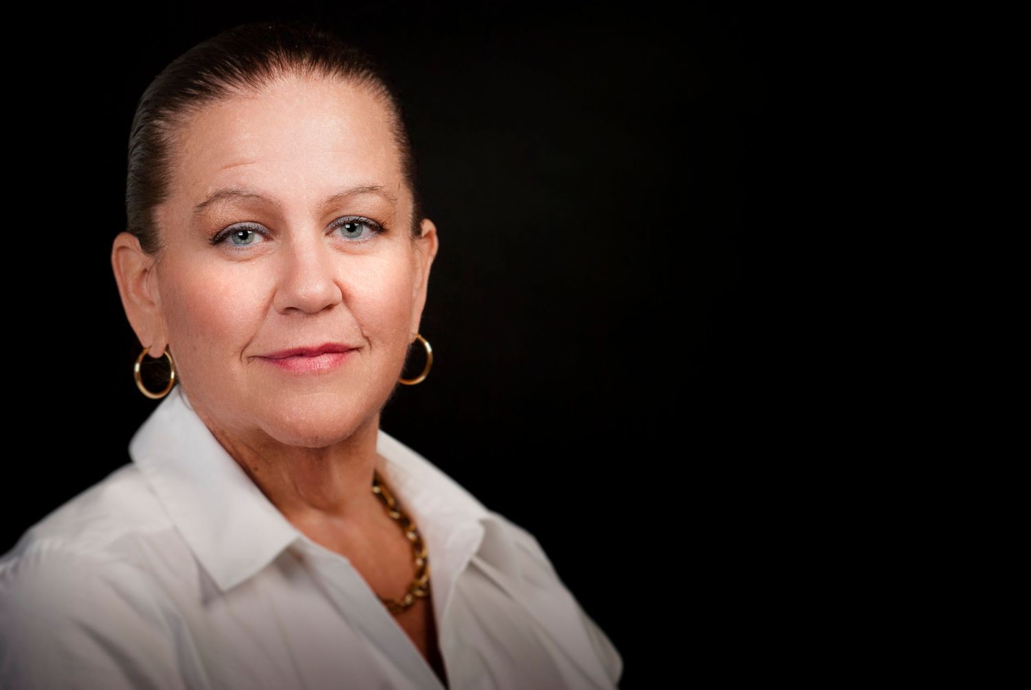 Professional headshot of Woman with white collar and necklace against black background.