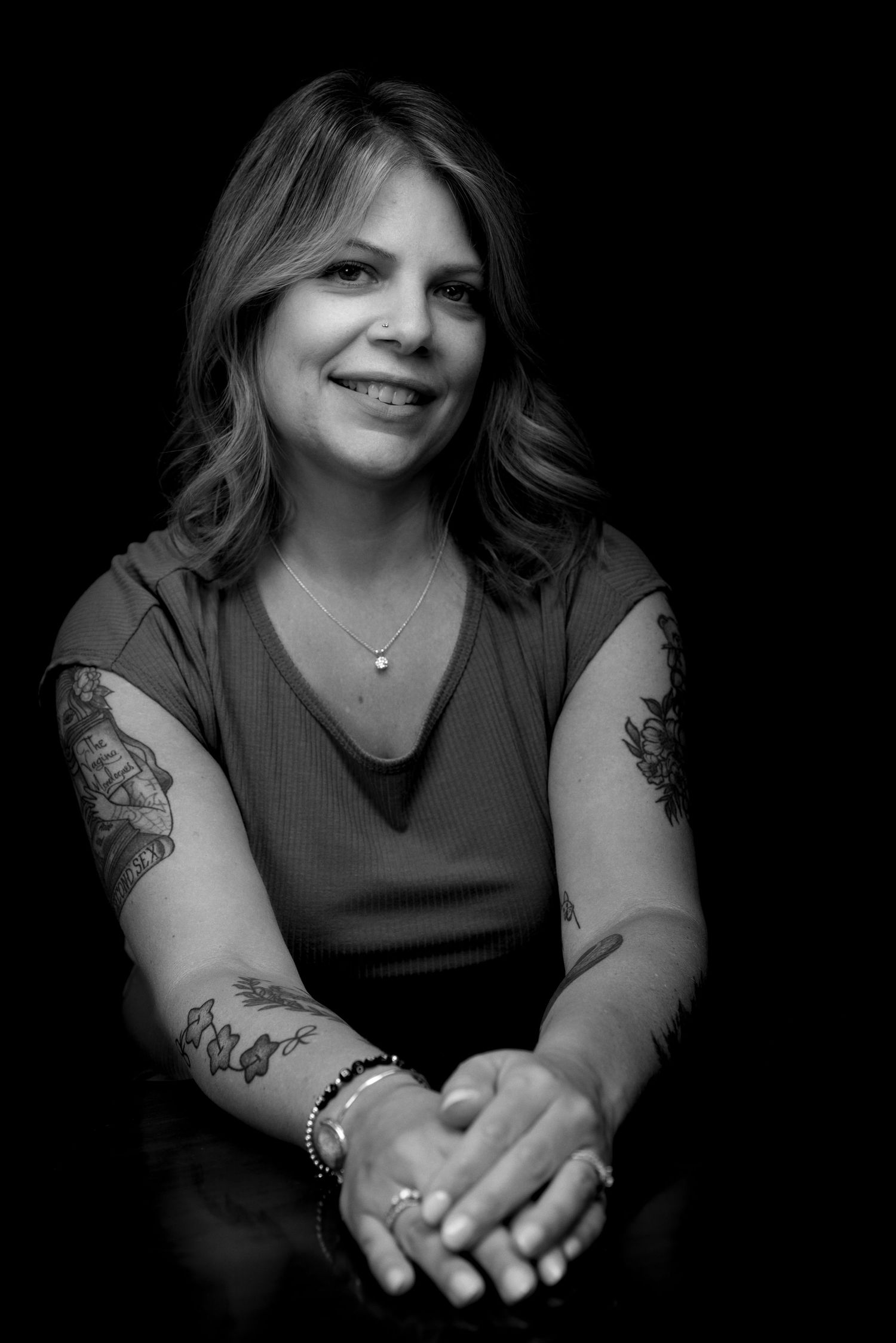 Artistic portrait showing tattooed arms and casual pose in dark clothing.